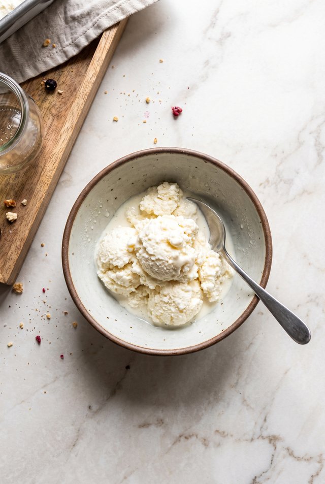 Overhead shot of two scoops of cottage cheese ice cream in a speckled bowl with a spoon resting against the rim