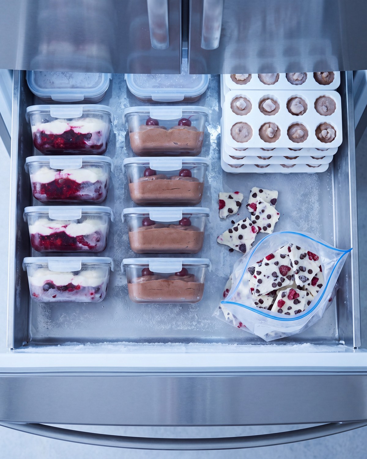 An open freezer drawer seen from above with portioned containers and pieces of frozen bark