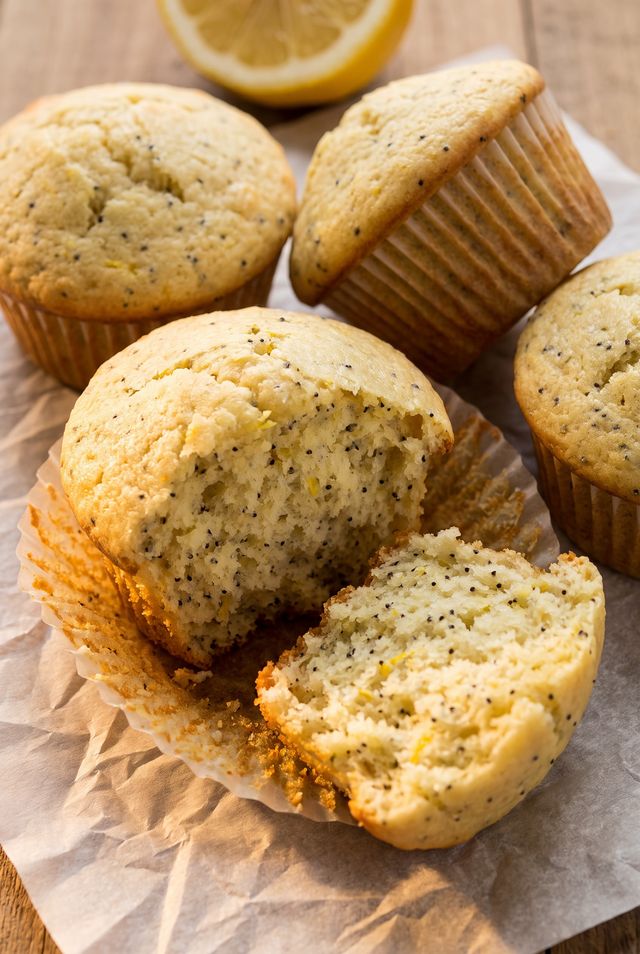 Unglazed lemon poppyseed muffins in paper liners, one torn in half showing poppy seeds and lemon zest in the crumb