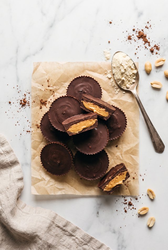 Protein peanut butter cups on parchment paper, three cut open to show the fudgy peanut butter filling, with peanuts and cocoa scattered nearby