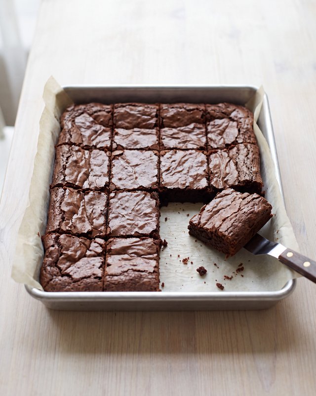 A pan of dark fudgy brownies cut into a grid of small squares on parchment, a knife beside it