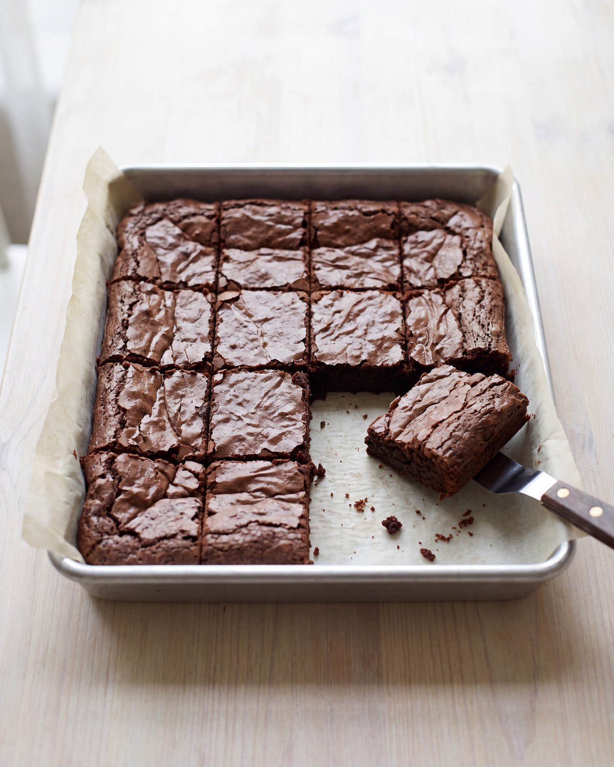 A pan of dark fudgy brownies cut into a grid of small squares on parchment, a knife beside it